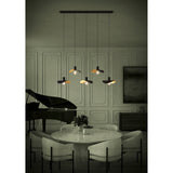 Saceda Linear Pendant Light in black and gold, five staggered hat-shaped shades with gold leaf undersides on a black bar, shown above a dining table.