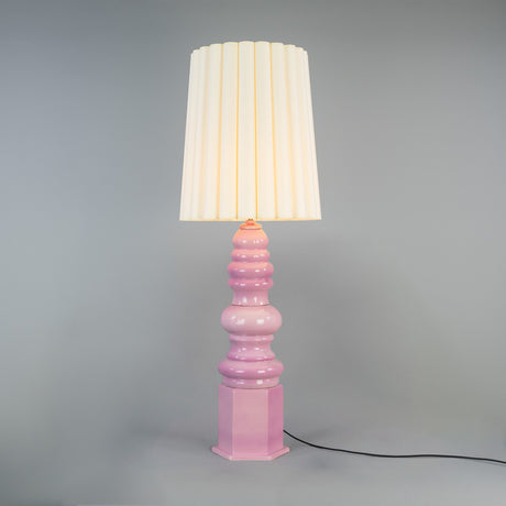 Safi Ceramic Table Lamp in glossy Carnation Pink with a tiered base on a hexagonal plinth, pale cream pleated fabric shade, satin brass fittings, set against a plain grey background.