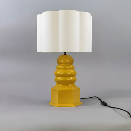 Safi Ceramic Table Lamp with a tiered Mustard Yellow glazed base on a hexagonal plinth, matt black fittings, and a white scalloped drum shade, shown against a plain grey background.