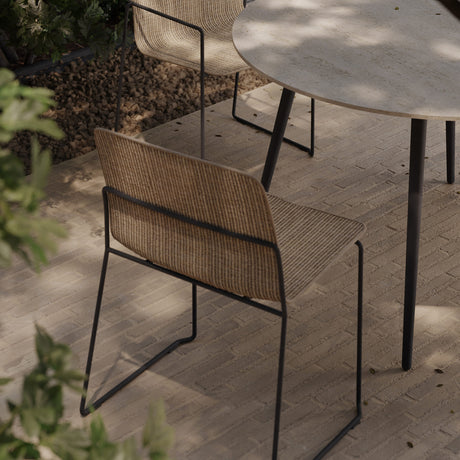 Sal Steel Stacking Garden Dining Chair with a slim black steel sled frame and woven sisal-look beige fabric seat and back, shown on an outdoor patio beside a round table.