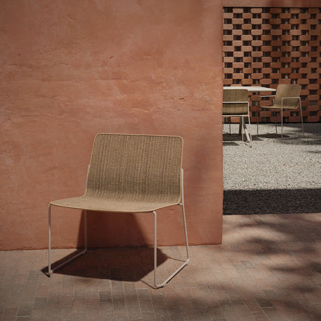 Sal steel stacking garden lounge chair with woven sisal-look beige seat and back on a slim sled base, shown on a patio beside a terracotta wall.