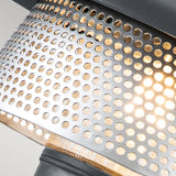 A close-up view of the Saturne 1 Light Outdoor Wall Light - Grey reveals circular perforations in its metal surface, reminiscent of a silver mesh diffuser that gently diffuses light. The texture and arrangement of these openings produce an intriguing visual effect, much like those seen in a modern outdoor wall light design. The background is softly illuminated.