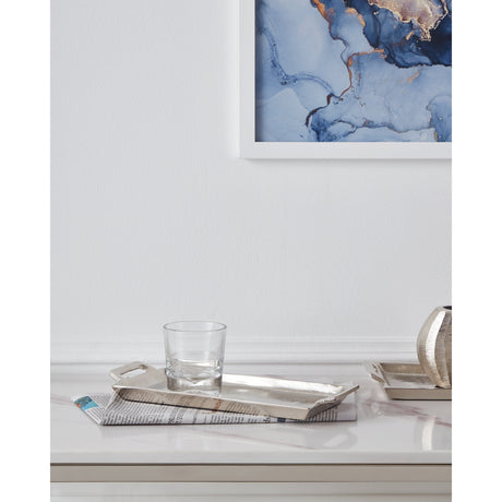 Savant Decorative Tray in nickel-finish aluminium with cut-out end handles, shown on a marble console table holding a glass tumbler, styled beneath a framed abstract artwork.