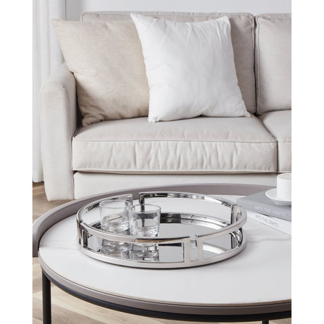 Savant Decorative Tray in silver, a round mirrored tray with a polished chrome open rectangular link rim, shown on a coffee table with glassware beside a beige sofa.