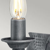 Close-up of a lit bulb in the Saxon 1 Light Wall Light, featuring a textured metal base and candle-like holder, enhanced by a wrought iron frame that exudes medieval aesthetics.