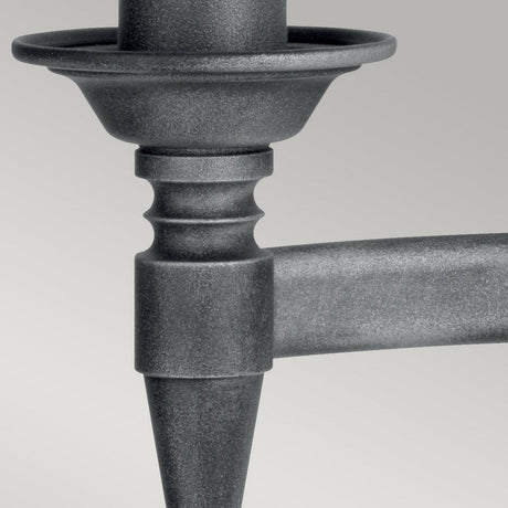 Close-up of the Saxon 2 Light Wall Light in a black/silver patina finish, showcasing its conical tip and circular disk with smooth and textured surfaces. The industrial design evokes the craftsmanship of wrought iron against a light gray background.