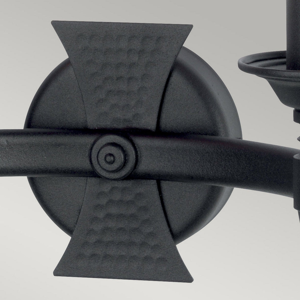 Detailed view of the Saxon 2 Light Wall Light - Black, featuring a medieval-inspired design with a textured circular base and decorative cross-shaped pattern. This black wrought iron fixture boasts a smooth, dark finish and is displayed against a light grey background.