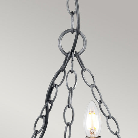 The Saxon 3 Light Chandelier in Black/Silver Patina presents a close-up view, showcasing its medieval charm with exposed bulbs. It features metal chains in a looped design hanging from the ceiling. Its illuminated bulbs provide warm lighting, seamlessly combining modern elegance against a neutral gray background.