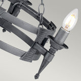 Close-up of the Saxon 3 Light Chandelier in black and silver patina, exuding medieval charm with its three exposed bulbs and decorative chains. Its pointed elements blend seamlessly with modern elegance, set against a soft gray background that highlights the chandelier's intricate details.