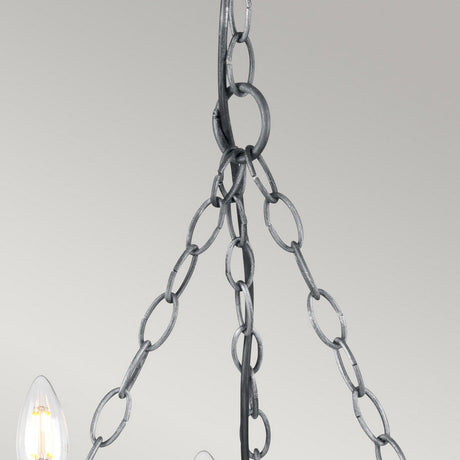 A close-up view showcases the wrought iron chain suspending the Saxon 5 Light Chandelier - Black/Silver Patina against a plain background. The image captures the intricate links and part of the chandelier's decorative light bulbs, all elegantly finished in black with a silver patina.