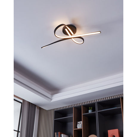 Selvina 1 LED flush ceiling light in black, its sculptural steel and aluminium ribbon with warm-white glow mounted on a white ceiling above shelving in a living space.