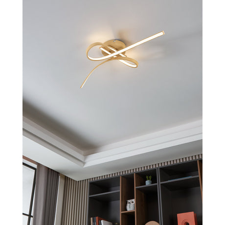 Selvina 2 LED flush ceiling light in light brown wood-effect finish, its looping ribbon-like arms stretching across a white ceiling above a living room shelving unit.