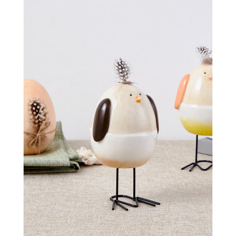 Sendayan bird ornament with cream and white egg-shaped body, glossy brown wings, orange beak, and spotted feather on top, standing on black wire legs, styled with eggs on a neutral tabletop.