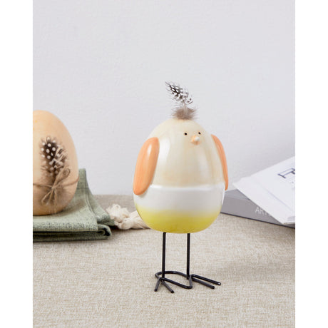 Sendayan Bird Ornament figurine with glossy egg-shaped body shading from pastel apricot to white to yellow, apricot wings and feather crest, on thin black legs, shown on a fabric surface.