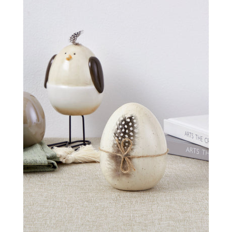 Sendayan ceramic decorative egg in speckled beige with a spotted feather and twine bow, displayed near a ceramic bird figurine and books.