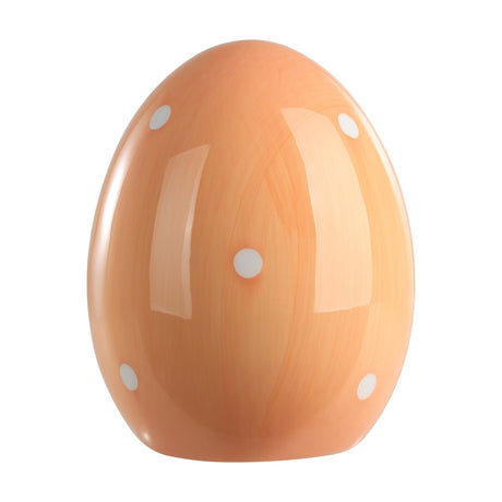 Sendayan ceramic decorative egg in pastel apricot with glossy finish and scattered white polka dots, flattened base for freestanding display, on a plain white background.