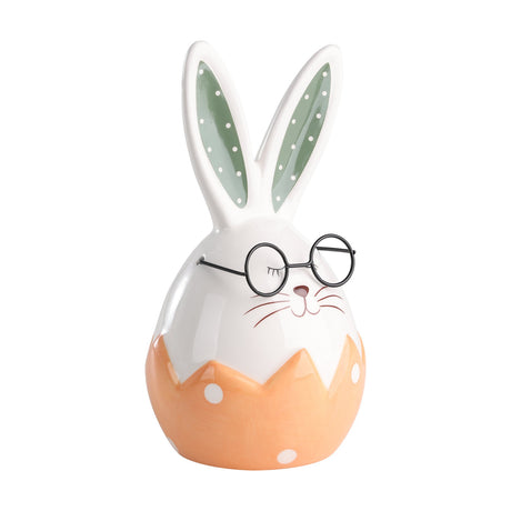 Ceramic rabbit ornament with egg-shaped white body in an orange polka-dot cracked eggshell, tall dotted ears, round black glasses, and a sleepy whiskered face on a white background.