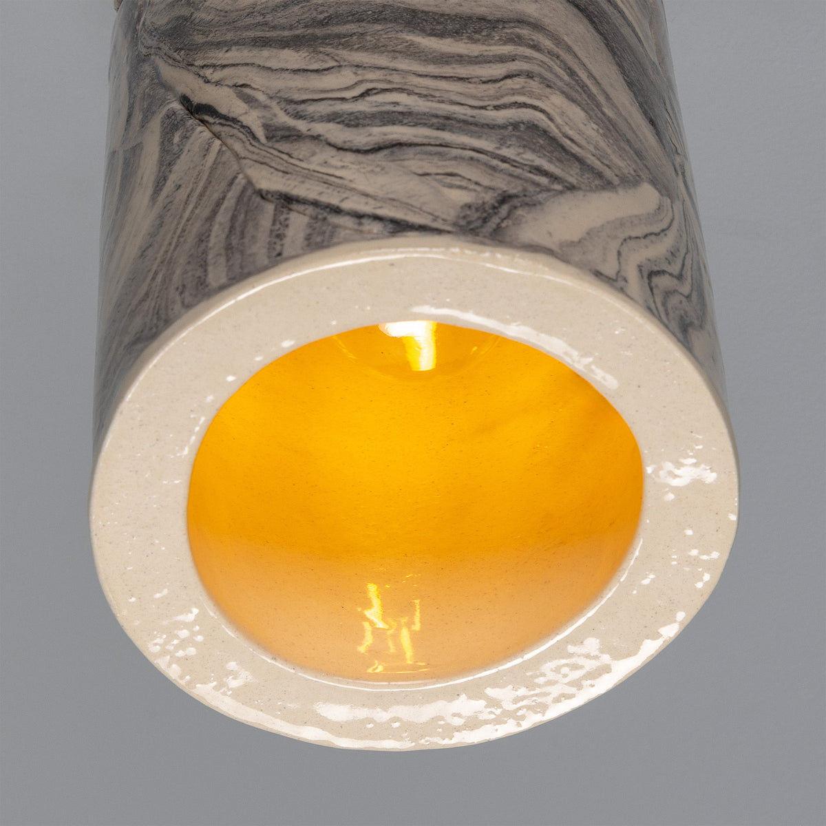 Senna Ceramic Ceiling Light in marbled grey and cream, close-up of the slim cylindrical shade's open base glowing amber around an E27 bulb.