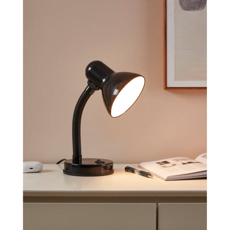 Sermessa Table Lamp in gloss black with dome shade, flexible gooseneck arm and round base, shown lit on a desk beside a book in a bedroom setting.