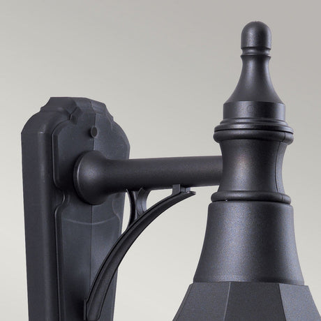 Close-up of the Shannon 1 Light Outdoor Down Wall Light in black, showcasing its decorative design with a smooth, matte finish. This corrosion-proof fixture features a curved arm and an ornate top detail. Its IP44 rating guarantees durability against the elements, set against a plain, light gray background.