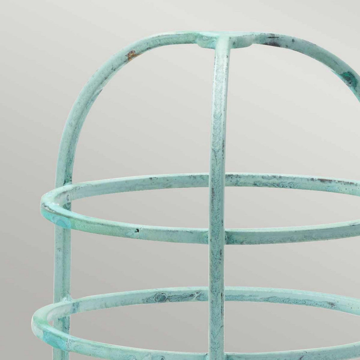 A close-up view of the Verdigris Cage Accessory for Sheldon & Somerton, featuring a turquoise metal wire frame with a rounded top and intersecting horizontal and vertical bars, set against a gradient light gray background.