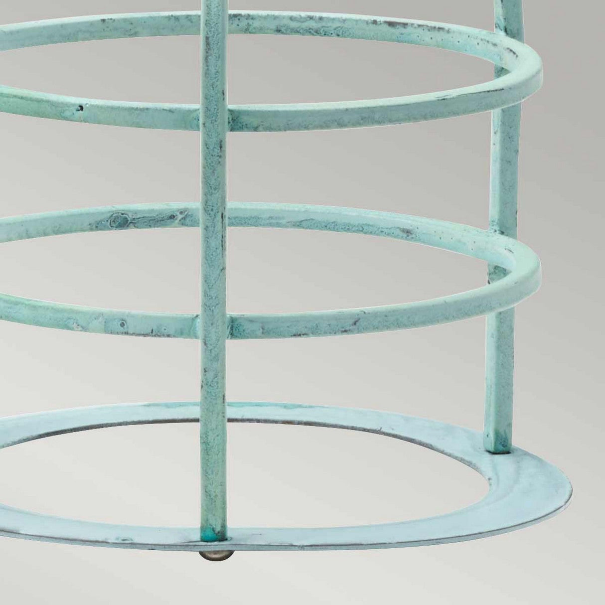 Close-up of the Cage Accessory for Sheldon & Somerton in a light turquoise hue with circular rings and vertical bars, reminiscent of verdigris-finished metalwork, set against a neutral gray background. The structure boasts a weathered patina, giving it a rustic, vintage appearance similar to aged brass lanterns.