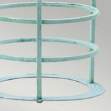 Close-up of the Cage Accessory for Sheldon & Somerton in a light turquoise hue with circular rings and vertical bars, reminiscent of verdigris-finished metalwork, set against a neutral gray background. The structure boasts a weathered patina, giving it a rustic, vintage appearance similar to aged brass lanterns.