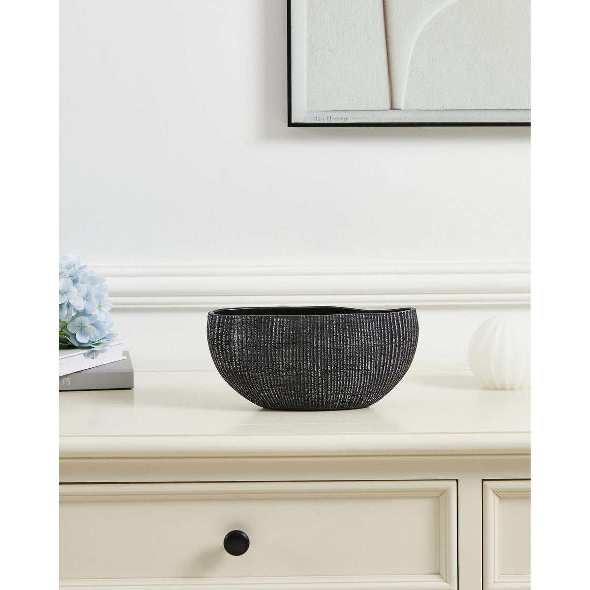 Shiguhe ceramic decorative bowl with an oval wavy rim and ribbed black and silver exterior, shown on a cream sideboard beside flowers and a framed print.