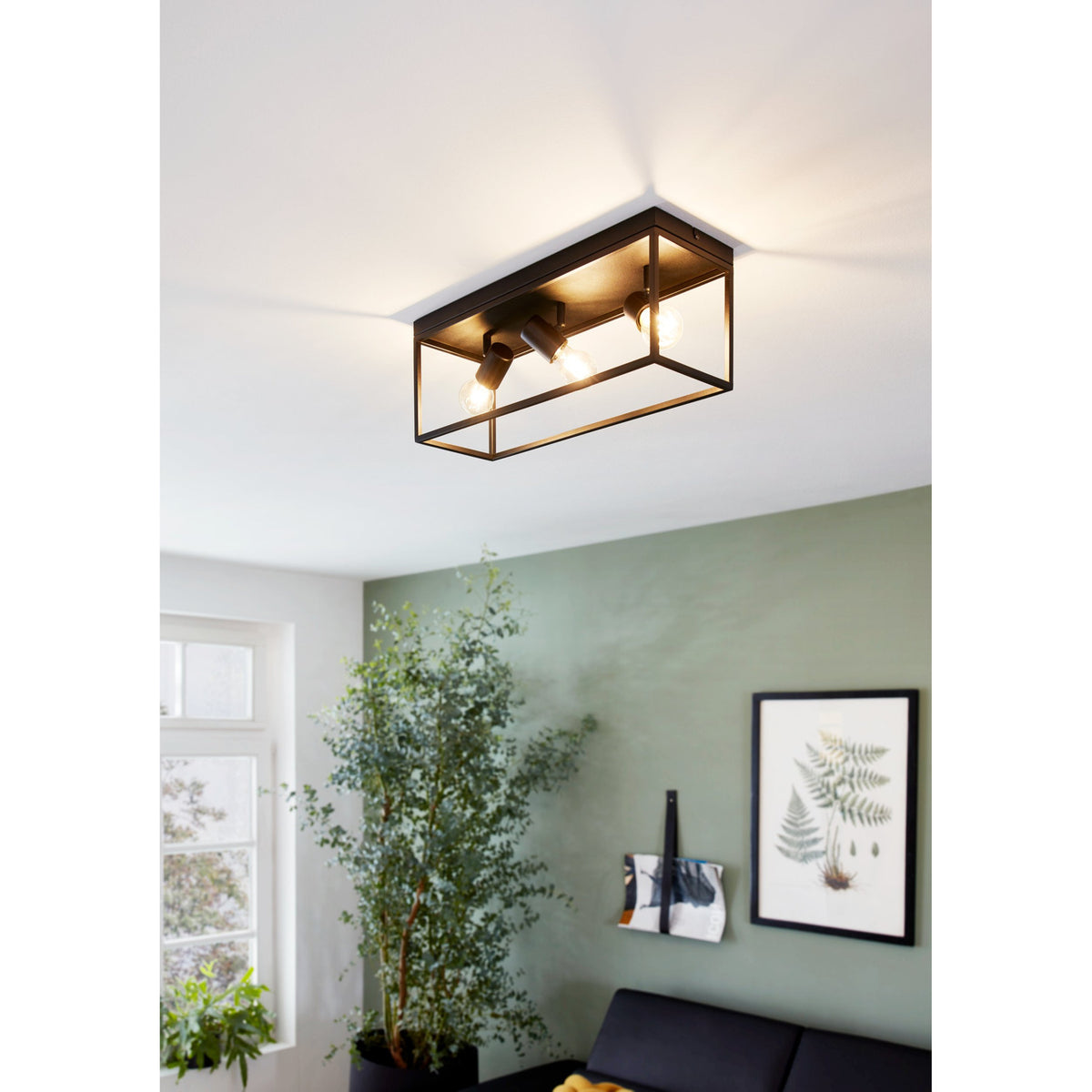 Silentina 3 Light Ceiling Light in black steel with an open rectangular frame and three adjustable spotlight heads, shown fitted to a white ceiling above a living room with a green wall.