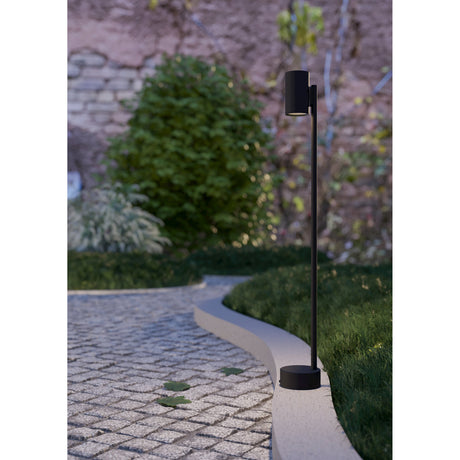 Silvessa Bollard Light in black, a slim steel post with a cylindrical GU10 head on a round base, standing beside a garden path and hedge.