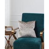 Singu Cushion in beige and brown with a raised velvety geometric fret pattern, shown on a teal velvet armchair in a living room setting.