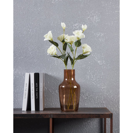 Siranana Glass Vase 25cm in Brown, bottle-shaped with rounded shoulders and narrow neck, holding white flowers, styled on a dark table beside books against a grey textured wall.