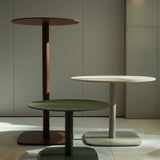 Sirkel Aluminium Outdoor Bar Table in red, white, and green, each with a round tabletop on a tall central leg and rounded square base, shown together indoors.
