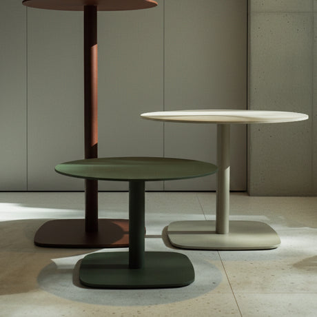 Sirkel round outdoor dining tables in green, white, and brown with aluminium pedestal legs and rounded square steel bases, shown indoors in varying heights.
