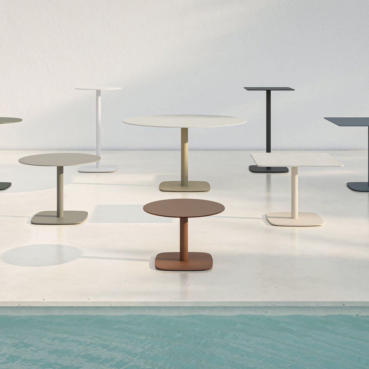 Sirkel round outdoor dining table in white, with aluminium pedestal leg and rounded square base, shown among various coloured Sirkel tables on a sunlit poolside terrace.