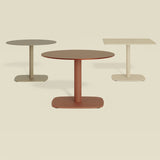 Sirkel Ø90cm round outdoor dining table in rust-red aluminium with central leg and rounded square base, shown with grey and ivory versions on a plain background.