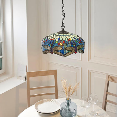Tiffany Alderworth Medium Pendant in blue leaded glass with dragonfly motif, hanging on a chain above a dining table with chairs and a vase.
