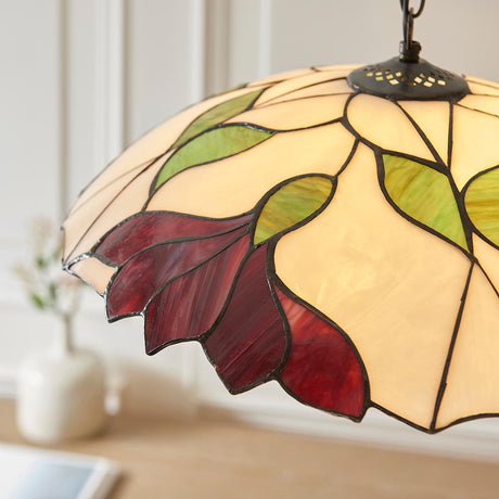 Amberhurst Large Tiffany pendant light with leaded stained glass shade in cream, green leaves and red petals, suspended above a wooden surface.
