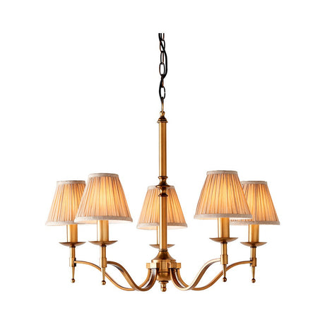 Interiors 1900 Ambledale 5 light chandelier in antique brass with curved arms and champagne pleated fabric shades, shown on a plain white background.