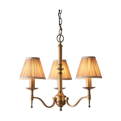 Interiors 1900 Ambledale 3 light pendant in antique brass with three curved arms, candle lamps and champagne pleated fabric shades on a white background.