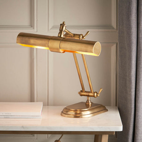 Interiors 1900 Larchdale two-light table lamp in solid antique brass with adjustable arms, sitting on a marble console beside books.