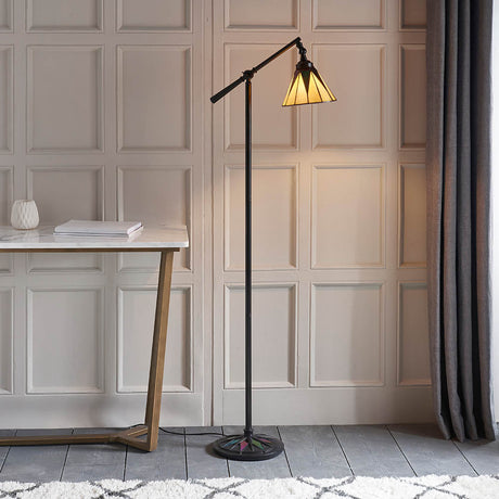 Tiffany Wistcombe Star Task floor lamp with multicoloured leaded glass shade and black metal arm, beside a marble desk against panelled walls.