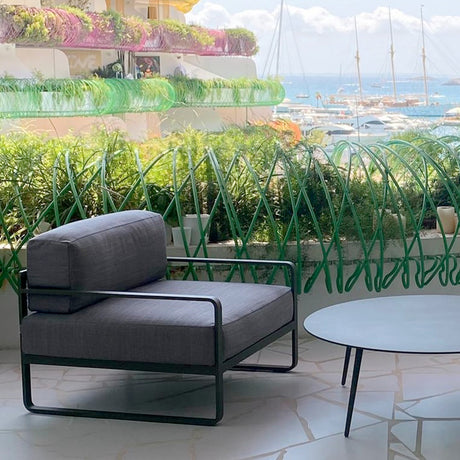 Sit aluminium garden armchair with dark grey cushions and black square-arm frame, shown on a terrace with sea and marina view.