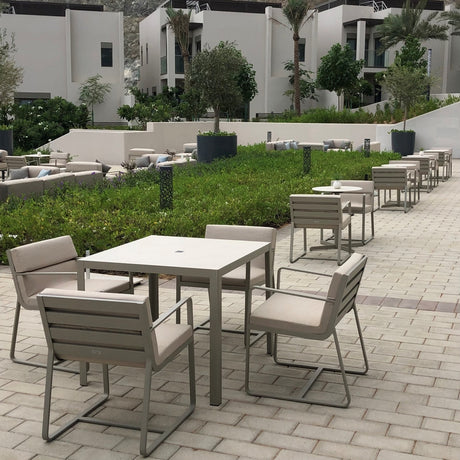 Sit aluminium garden dining armchairs with beige cushions and sled-leg frames, arranged around square tables on an outdoor patio.