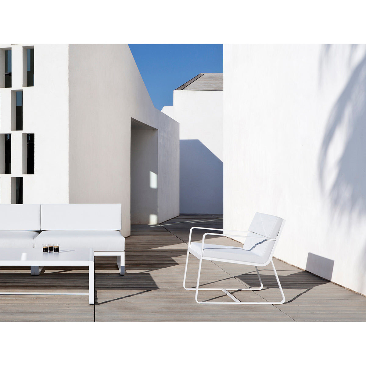 Sit Aluminium Garden Lounge Chair in white, with sled legs and flat arms, shown with cushions on a terrace beside a matching sofa and coffee table.