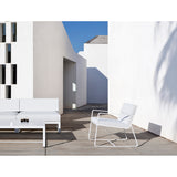 Sit Aluminium Garden Lounge Chair in white, with sled legs and flat arms, shown with cushions on a terrace beside a matching sofa and coffee table.
