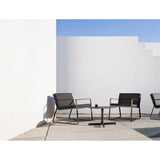 Sit Aluminium Garden Lounge Chairs with black cushions and sled legs, shown on a terrace beside a round side table against a white wall.