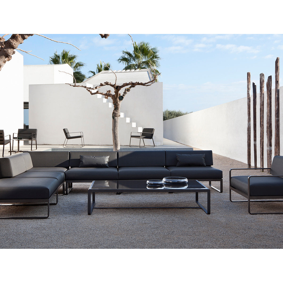 Sit Aluminium Modular Garden Sofa centre module in anthracite, shown as part of an L-shaped outdoor sofa with dark cushions in a sunny courtyard setting.