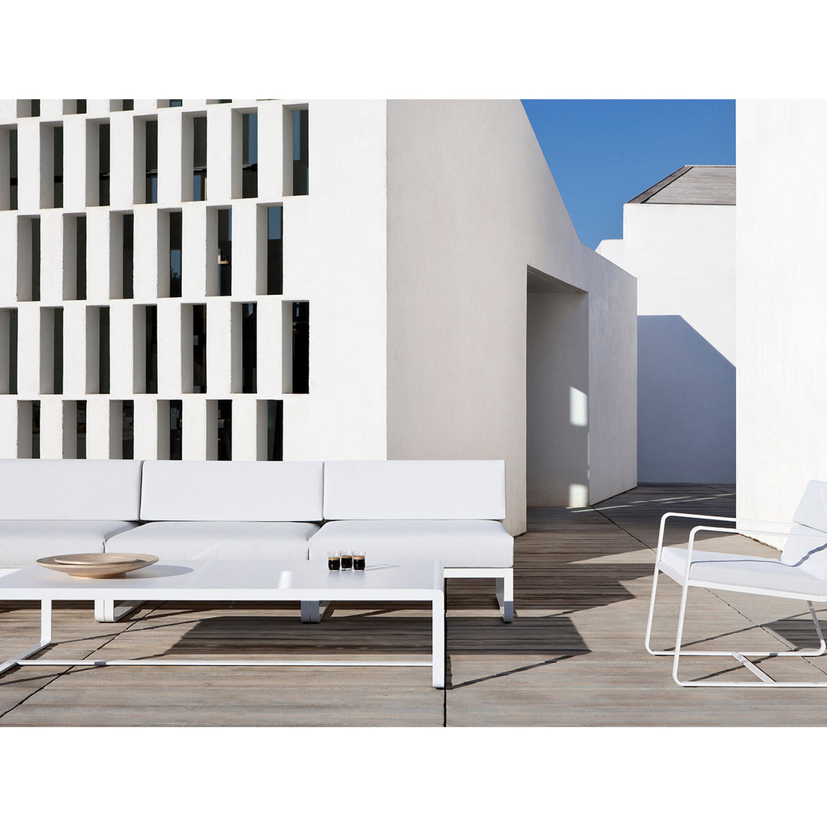 Sit Aluminium Modular Garden Sofa centre module in white with cushions, armless design on a rooftop terrace beside a matching coffee table and lounge chair.
