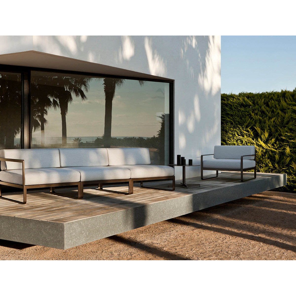 Sit Aluminium Modular Garden Sofa with left arm module and cream cushions, shown on an outdoor terrace with bronze-finished aluminium sled-leg frame.